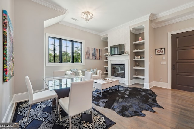 dining room with a brick fireplace, visible vents, crown molding, and wood finished floors