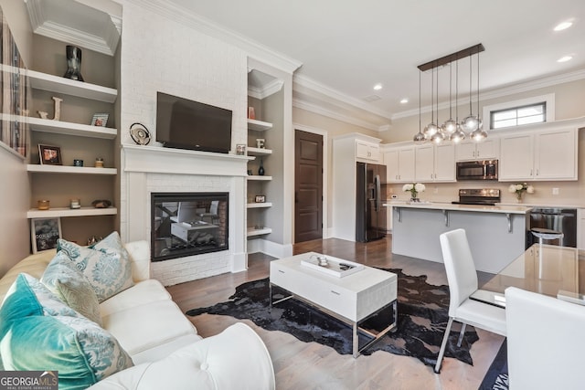 living room featuring built in features, dark wood-type flooring, crown molding, a brick fireplace, and recessed lighting