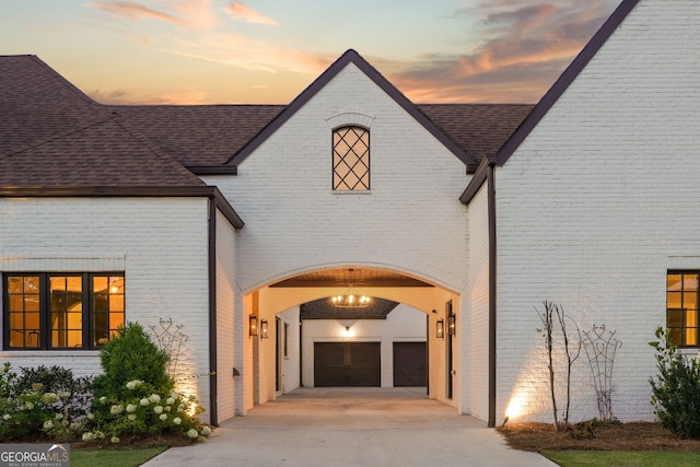 view of exterior entry featuring a garage, concrete driveway, brick siding, and roof with shingles