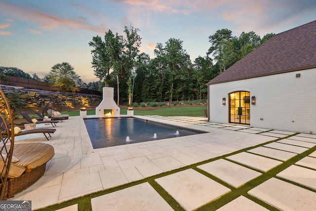 view of swimming pool featuring a warm lit fireplace, a patio area, and fence