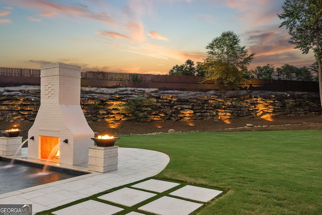 yard at dusk with a warm lit fireplace and a patio