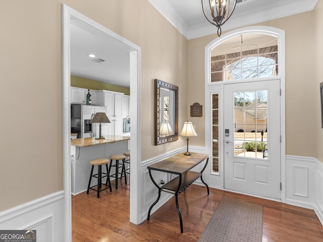 entryway with a wainscoted wall, crown molding, visible vents, wood finished floors, and a chandelier