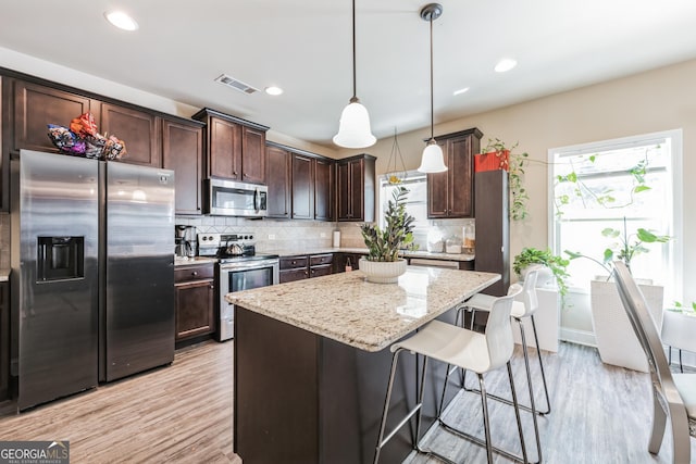 kitchen with pendant lighting, decorative backsplash, dark brown cabinetry, light stone counters, and stainless steel appliances