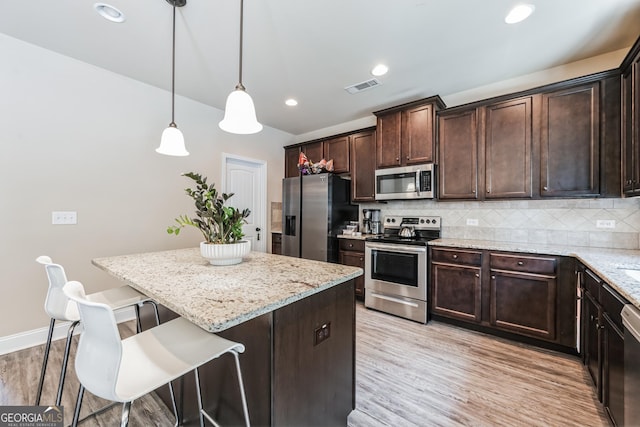 kitchen with appliances with stainless steel finishes, dark brown cabinets, a kitchen breakfast bar, tasteful backsplash, and decorative light fixtures