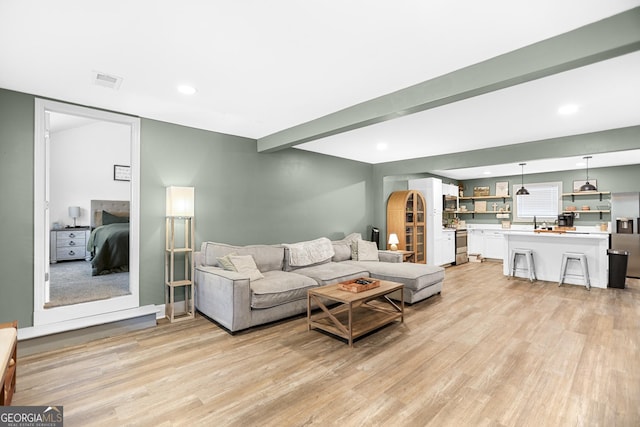 living room featuring sink, beam ceiling, and light hardwood / wood-style flooring