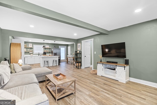 living room featuring sink, light hardwood / wood-style flooring, and beamed ceiling