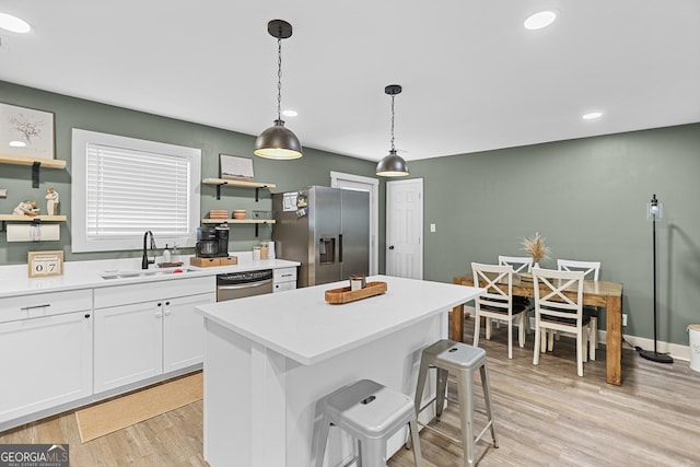 kitchen featuring sink, hanging light fixtures, stainless steel appliances, white cabinets, and a kitchen island