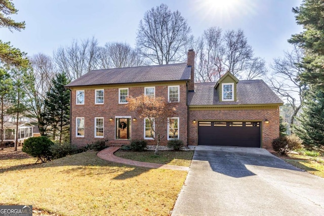 view of front facade with driveway, brick siding, a chimney, an attached garage, and a front yard