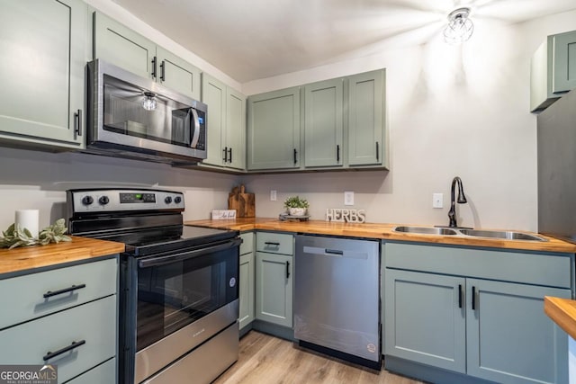 kitchen with stainless steel appliances, sink, wooden counters, and light hardwood / wood-style flooring