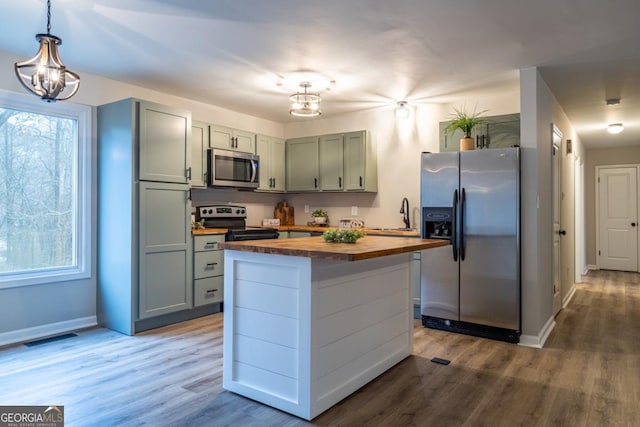 kitchen featuring appliances with stainless steel finishes, butcher block counters, hanging light fixtures, wood-type flooring, and a kitchen island