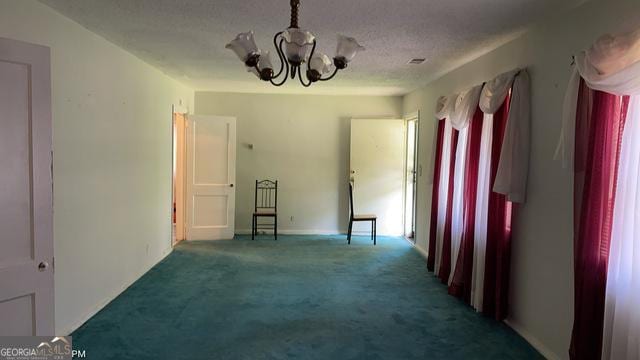 carpeted empty room with a chandelier and a textured ceiling