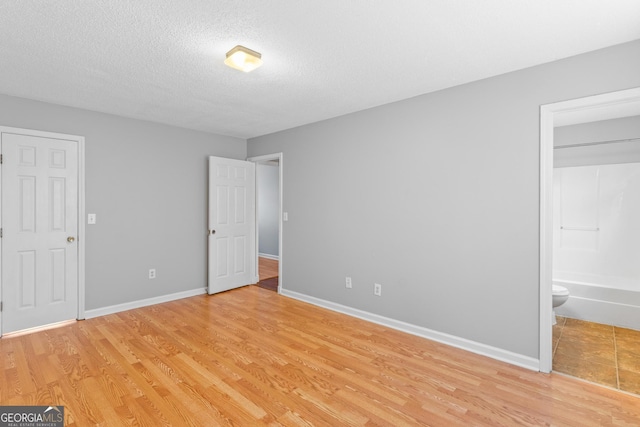 unfurnished bedroom with connected bathroom, light hardwood / wood-style flooring, and a textured ceiling