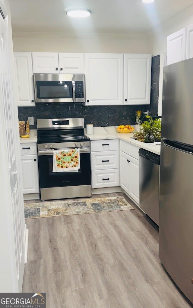 kitchen featuring tasteful backsplash, white cabinetry, stainless steel appliances, crown molding, and light wood-type flooring