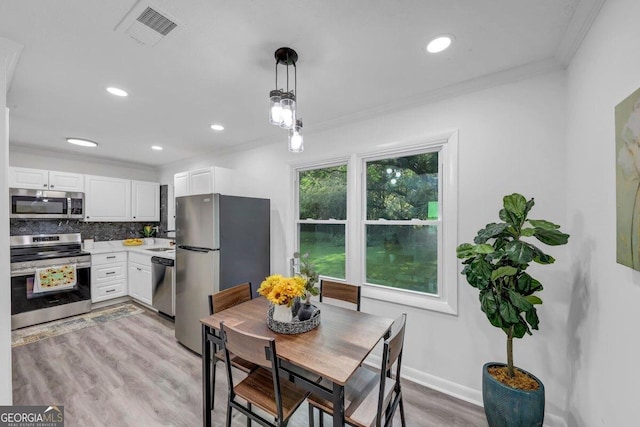 kitchen featuring crown molding, appliances with stainless steel finishes, pendant lighting, light hardwood / wood-style floors, and white cabinets