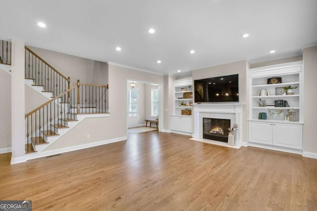 unfurnished living room with built in features, ornamental molding, and light hardwood / wood-style floors