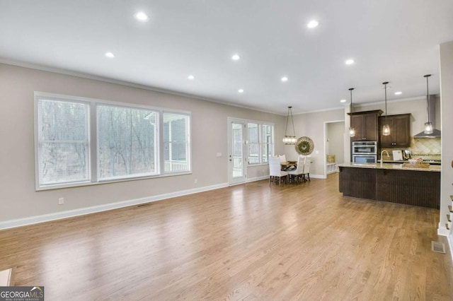 kitchen with decorative backsplash, hanging light fixtures, wall chimney exhaust hood, dark brown cabinets, and light hardwood / wood-style flooring