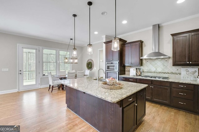 kitchen featuring dark brown cabinetry, wall chimney exhaust hood, decorative light fixtures, and an island with sink