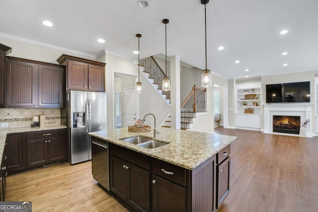 kitchen featuring sink, decorative light fixtures, dark brown cabinets, stainless steel appliances, and light stone countertops