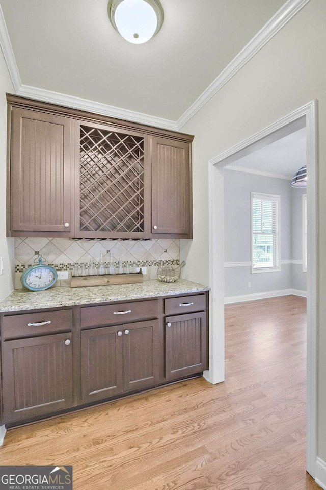 bar featuring crown molding, dark brown cabinets, tasteful backsplash, light stone countertops, and light hardwood / wood-style floors