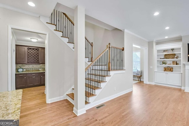 staircase featuring wood-type flooring, ornamental molding, and built in shelves