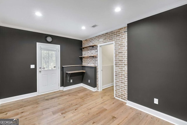 unfurnished living room featuring crown molding, brick wall, and light hardwood / wood-style floors