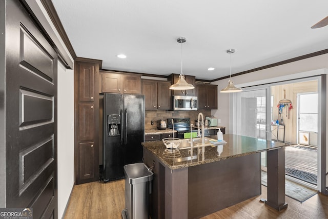 kitchen with wood-type flooring, hanging light fixtures, dark stone countertops, a center island with sink, and black appliances