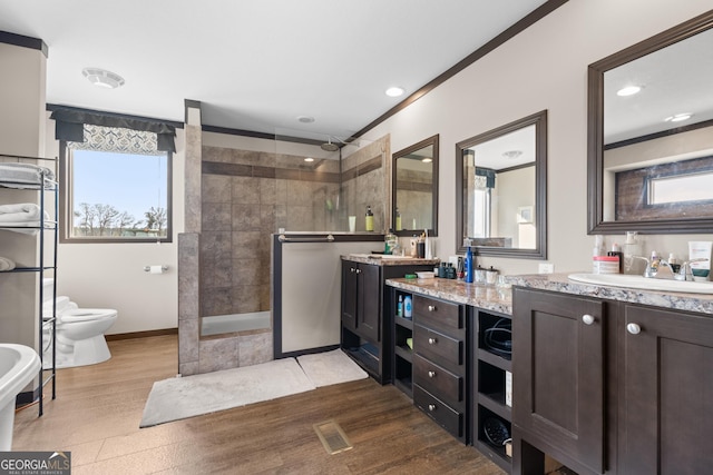 bathroom featuring tiled shower, vanity, wood-type flooring, ornamental molding, and toilet