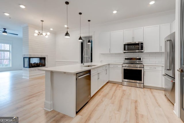 kitchen featuring pendant lighting, sink, white cabinets, kitchen peninsula, and stainless steel appliances