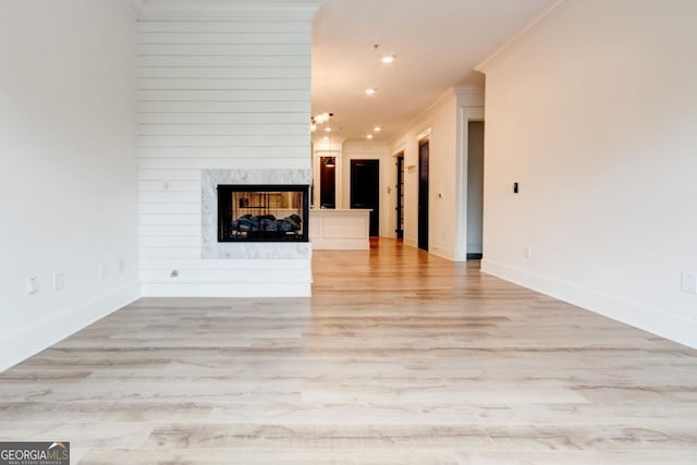 unfurnished living room with crown molding, a premium fireplace, and light hardwood / wood-style floors