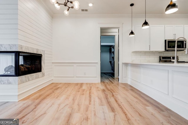 unfurnished living room with a notable chandelier, a high end fireplace, ornamental molding, and light wood-type flooring