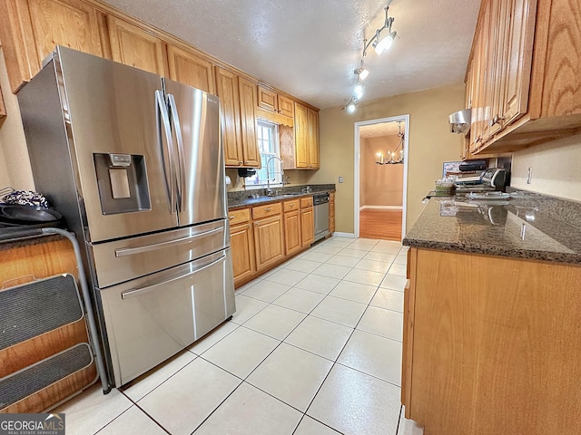 kitchen featuring sink, appliances with stainless steel finishes, dark stone countertops, a textured ceiling, and light tile patterned flooring