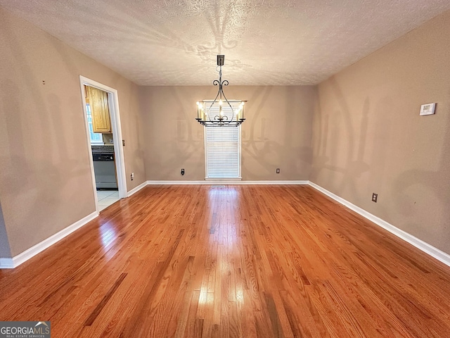 unfurnished dining area with a chandelier, a textured ceiling, and light wood-type flooring