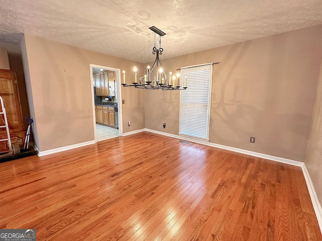 unfurnished dining area featuring a chandelier, light hardwood / wood-style flooring, and a textured ceiling