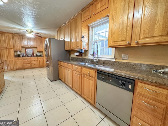 kitchen featuring sink, light tile patterned floors, ceiling fan, appliances with stainless steel finishes, and dark stone countertops