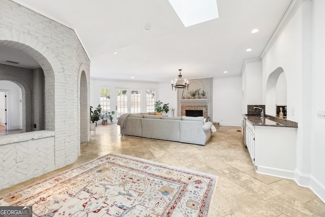 living room featuring crown molding, a skylight, an inviting chandelier, and a brick fireplace