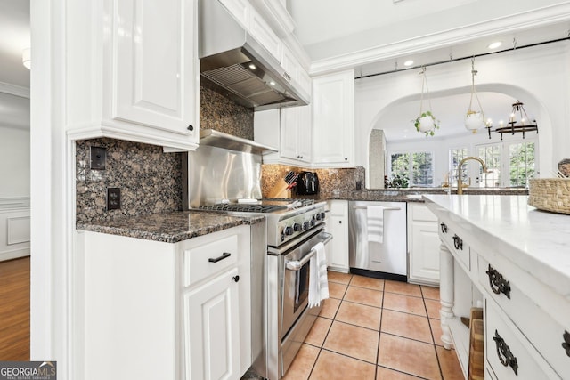 kitchen with wall chimney exhaust hood, dark stone countertops, pendant lighting, stainless steel appliances, and white cabinets