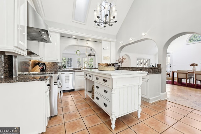 kitchen with appliances with stainless steel finishes, a kitchen island, range hood, white cabinetry, and hanging light fixtures