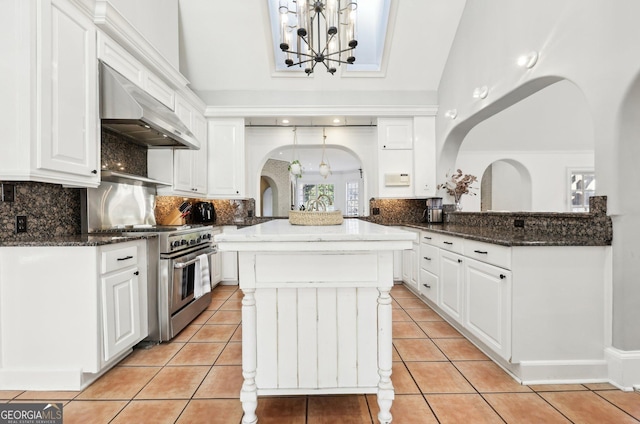 kitchen featuring high end stove, white cabinets, light tile patterned floors, kitchen peninsula, and wall chimney exhaust hood