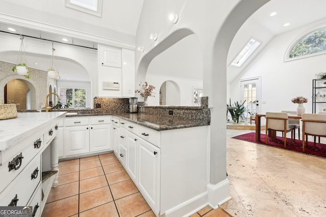 kitchen featuring high vaulted ceiling, tasteful backsplash, dark stone countertops, white cabinets, and hanging light fixtures