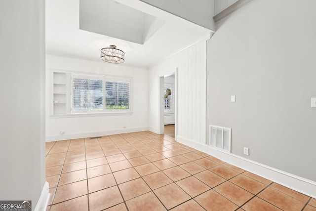 tiled empty room with built in features and a notable chandelier