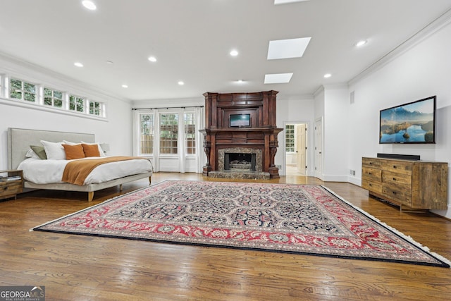 bedroom featuring hardwood / wood-style floors, crown molding, a skylight, and a large fireplace