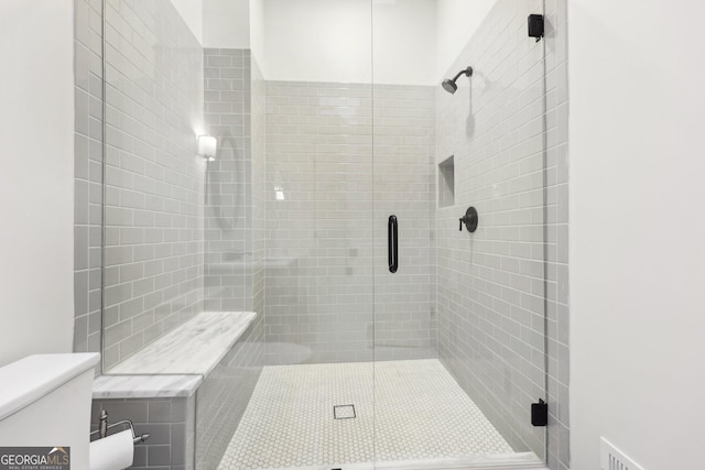 bathroom featuring a shower with door and toilet