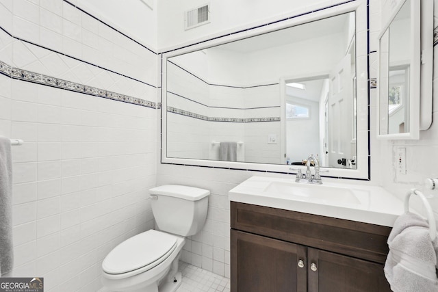 bathroom featuring vanity, toilet, and tile walls