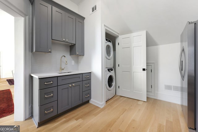 clothes washing area featuring stacked washer and clothes dryer, light hardwood / wood-style floors, and sink