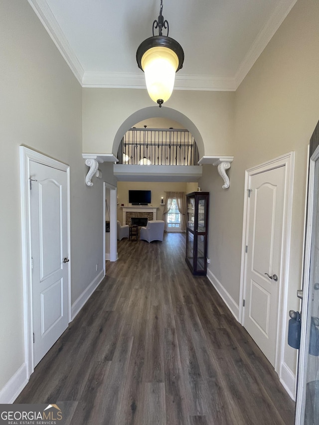 entryway with arched walkways, ornamental molding, and dark wood-style flooring