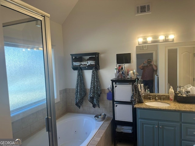 bathroom featuring vanity, tiled bath, and vaulted ceiling