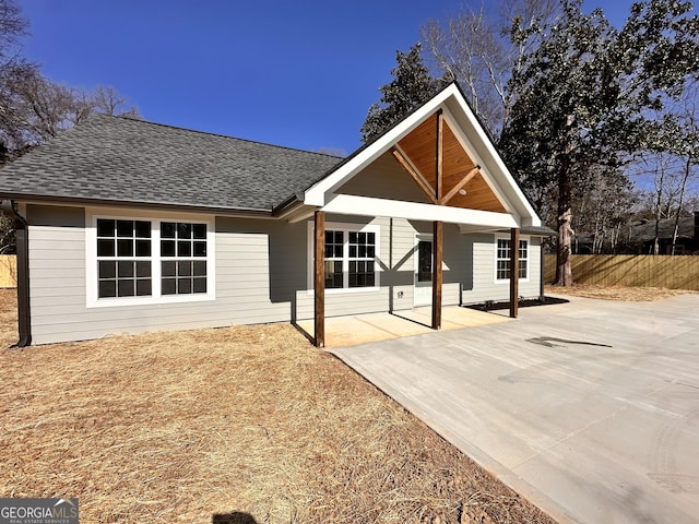 view of front of property featuring a shingled roof, a patio area, and fence