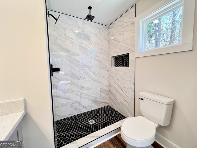 bathroom featuring tiled shower, toilet, vanity, plenty of natural light, and hardwood / wood-style floors