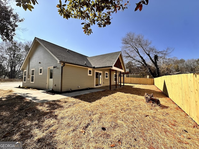 view of side of home featuring roof with shingles, a patio area, and a fenced backyard