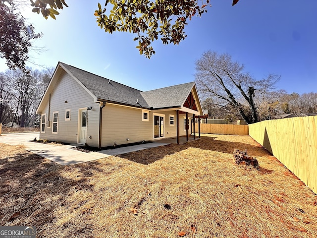 view of side of property featuring a patio, roof with shingles, and a fenced backyard